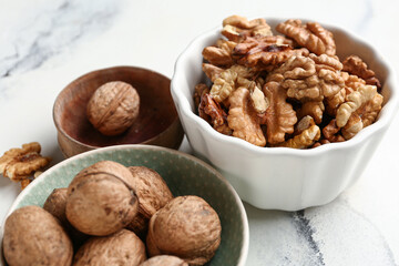 Bowls of tasty walnuts on white marble background