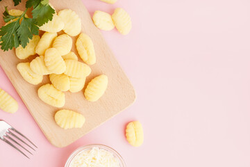 Wooden board with tasty gnocchi, grated cheese and parsley on pink background