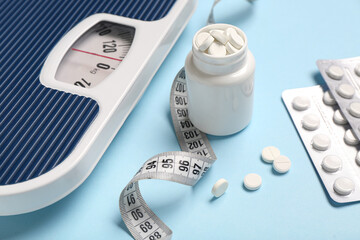 Bottle with weight loss pills, scales and measuring tape on blue background