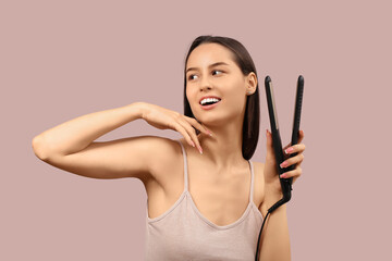 Fototapeta premium Beautiful young woman with hair straightener on pink background