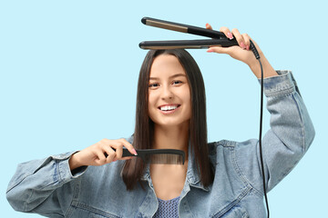 Obraz premium Beautiful young woman with hair straightener and comb on blue background