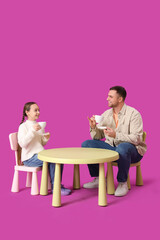 Fototapeta premium Father and his daughter having tea party on pink background