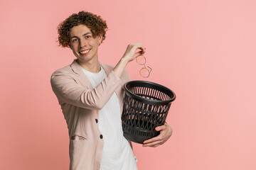 Caucasian young man with curly hair taking off throwing out glasses into bin after medical vision...
