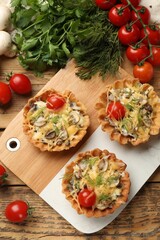 Tasty tartlets with cheese, tomatoes, mushrooms and dill on wooden table, flat lay