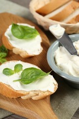 Delicious sandwiches with cream cheese and basil leaves on wooden table, closeup