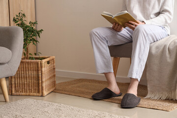 Man with book in slippers sitting on soft bench in room