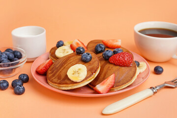 Tasty pancakes with blueberries and banana on orange background