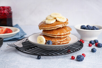 Plate on grate with tasty pancakes, banana slices and cutlery on white table