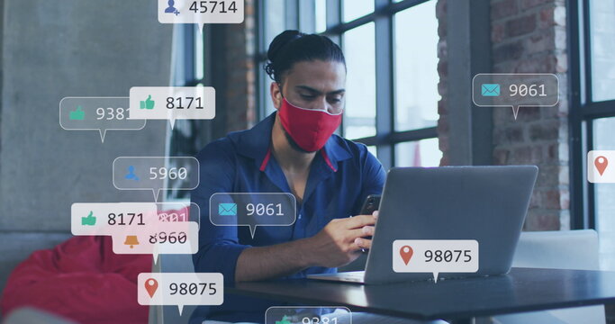 Image of social media icons and numbers over biracial businessman in face mask with laptop