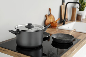 Electric stove with cooking pot and frying pan on wooden kitchen counter