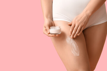 Beautiful young woman with jar of anti-cellulite cream on pink background, closeup