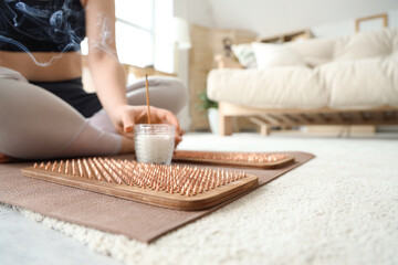 Sporty young woman with aroma stick and Sadhu board at home, closeup