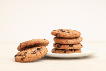 Plate of sweet cookies with chocolate chips on white background