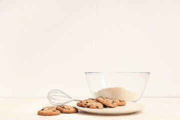 Plate of sweet cookies with chocolate chips and bowl of flour on white background