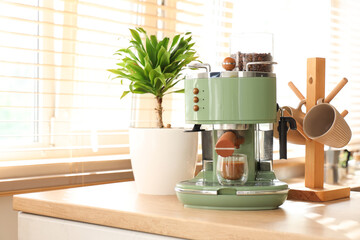 Modern coffee machine with cup of cappuccino on table in kitchen