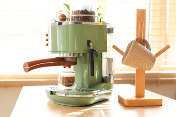 Modern coffee machine with cup of cappuccino on table in kitchen