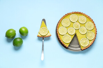 Plate and spatula with tasty lime tart on blue background