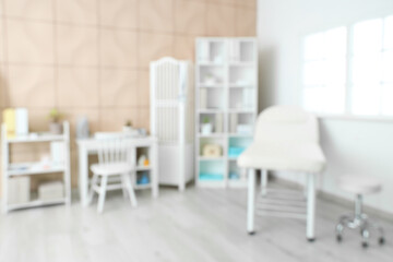 Blurred view of medical office with couch, doctor's workplace and shelf units