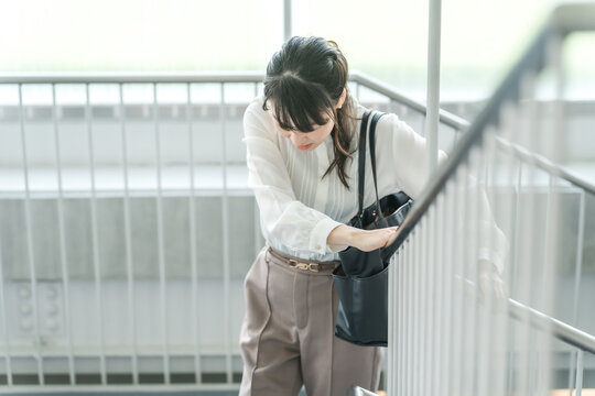 苦しみながら階段を登るビジネスウーマン（ぎっくり腰・腰痛・腹痛・膝痛）
