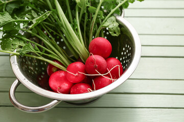 Colander with fresh radishes on green wooden background