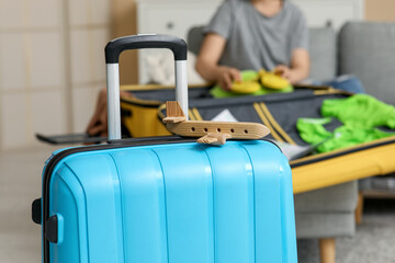 Blue suitcase near young woman in hat on sofa. Summer travel concept