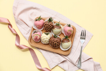 Wooden board with chocolate covered strawberries on yellow background