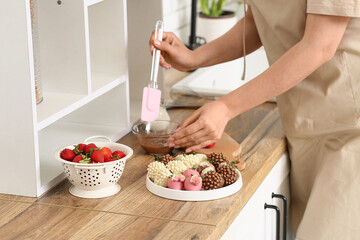 Beautiful young woman preparing chocolate covered strawberries at home