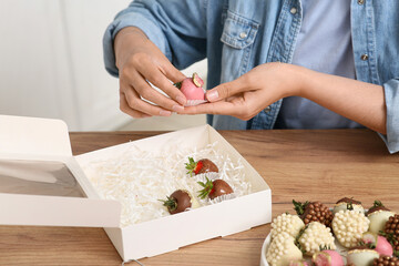 Young woman putting chocolate covered strawberries into box at home