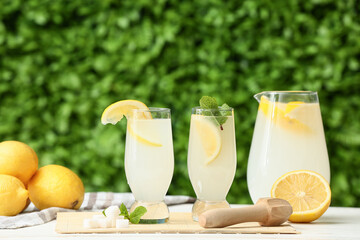 Glasses and jug of fresh lemonade with mint on white wooden table outdoors