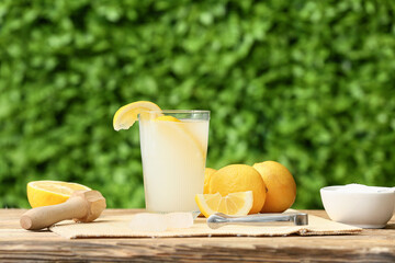Glass of fresh lemonade and juicer on wooden table outdoors