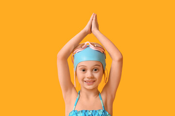Cute little girl in swimsuit, swimming hat and goggles on yellow background