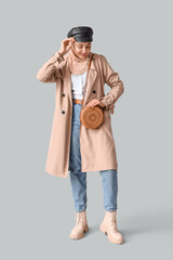 Stylish Muslim woman in trench coat on light background