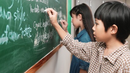 Side view of asian boy writing engineering prompt and programing system while standing blackboard...
