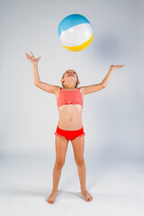 Happy young girl in swimsuit playing with a beach ball 