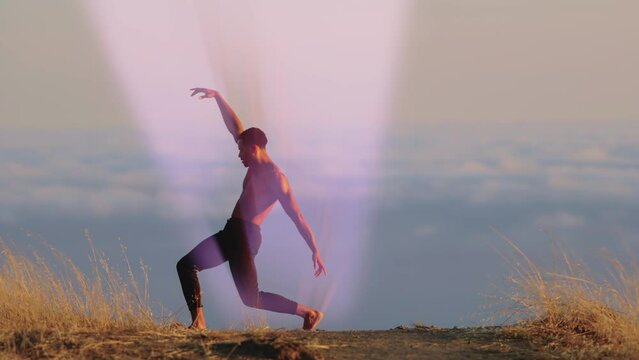 Male ballet dancer doing a choreographic dance move standing on a rock at sunset. Heavenly clouds are in the background and rays of light are coming from his body.