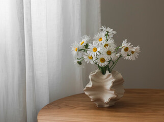 A bouquet of daisies in a ceramic creative vase on a round wooden table in the living room