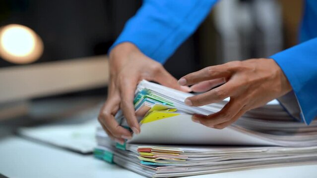 Businesswoman hands working in Stacks of paper files for searching and checking unfinished document achieves on folders papers at busy work desk office.