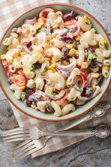 Southwestern pasta salad is a zesty summer side filled with fresh corn, onion, beans, peppers with creamy homemade ranch style dressing closeup on the bowl on the table. Vertical top view from above