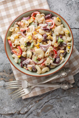 Southwestern elbow pasta salad with grilled corn, onion, beans, peppers with creamy dressing closeup on the bowl on the table. Vertical top view from above