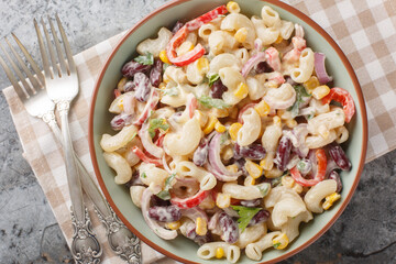 Delicious American macaroni pasta salad with onions, corn, beans, peppers with ranch dressing close-up in a bowl on the table. Horizontal top view from above