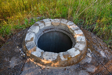 Old concrete sewer manhole with an open hatch without a lid. A large round hole leads underground to communications