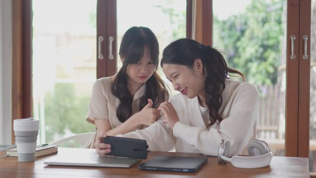 Two Asian university female friends are taking a break from studying to take a selfie with a smartphone to capture good memories at their home