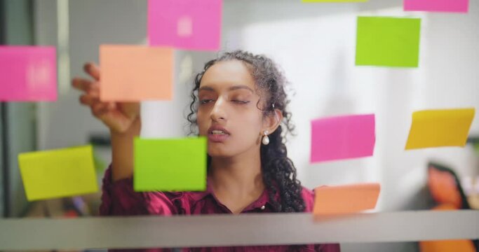 Close up of boss young adult lady read new notes look task data day time office glass wall board Indian gen z curly hair teen expert female girl check ideas plan list puts sticky paper job work place