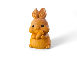 Miniature wooden rabbit holding a carrot on a white background