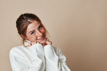 Fashionable young woman in white sweater posing for a photo on neutral background for beauty and fashion concept