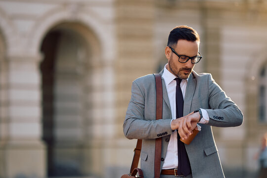 Mid adult businessman checking  time on wristwatch on street.