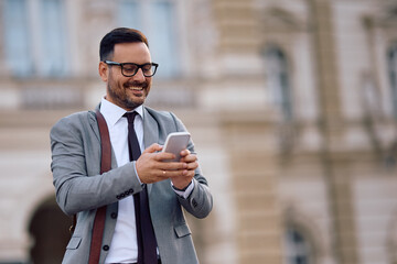 Happy businessman using app on mobile phone on city street.