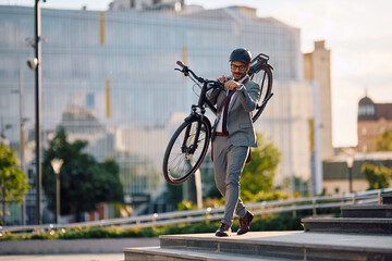 Naklejka premium Businessman carrying his bike down the stairs in city.