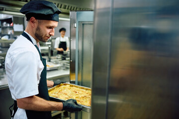 Professional cook using oven while preparing food in restaurant.