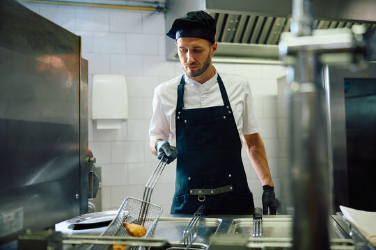 Male cook preparing food in deep fryer in  kitchen.
